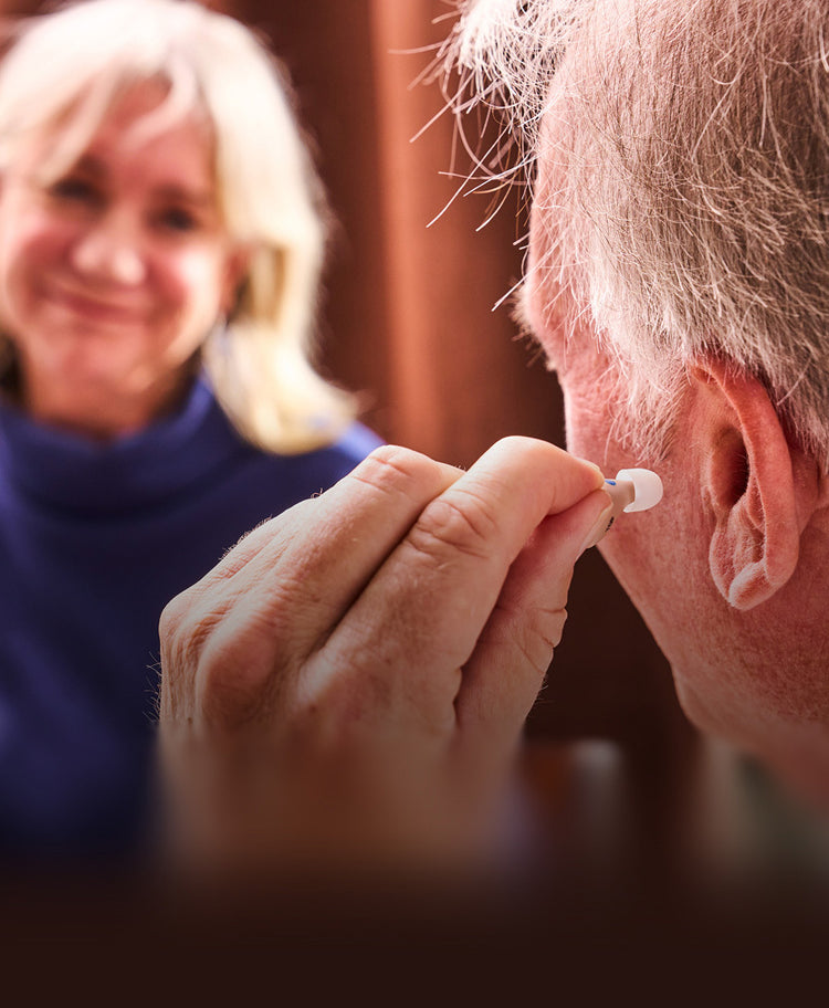 Person inserting a hearing aid into an elderly person's ear with a blurred background